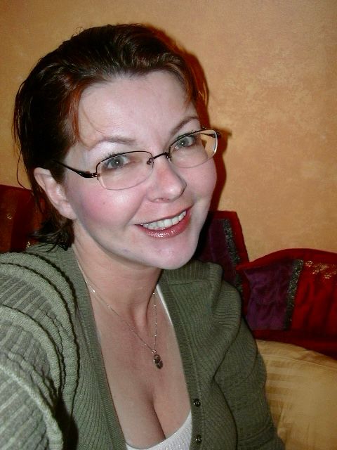 Woman wearing glasses and a green sweater, smiling up at camera. 