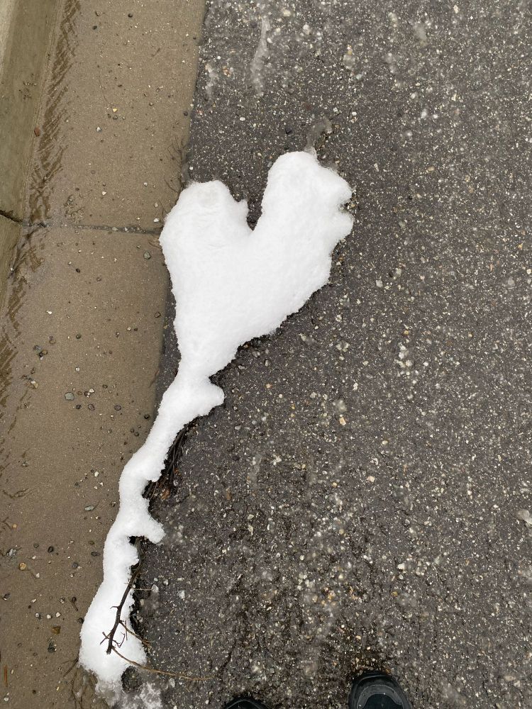 Snow on pavement in the shape of a balloon heart. 