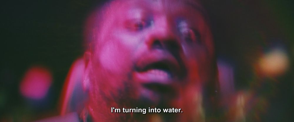 A frame from Godzilla X Kong: The New Empire (2024).
We see a (blurry) shot of a man, sitting in a chair of a vehicle of some kind. He is bathed in bisexual lighting, his eyes wide with shock. 
The caption reads, "I'm turning into water."

Not pictured: Godzilla; Kong; water
