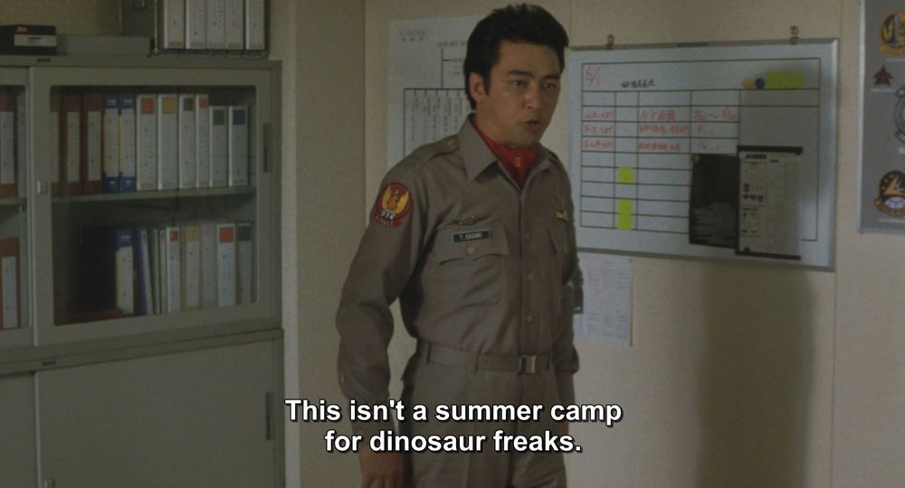 A frame from Godzilla vs Mechagodzilla II (1993).
A man in a military-ish mechanic(?) tan jumpsuit stands in an office. There are binders and whiteboard schedules on the walls in the background. 
The caption reads, "This isn't a summer camp for dinosaur freaks."

Not pictured: Godzilla; Mechagodzilla; the summer camp for dinosaur freaks, which I'm sure does exist
