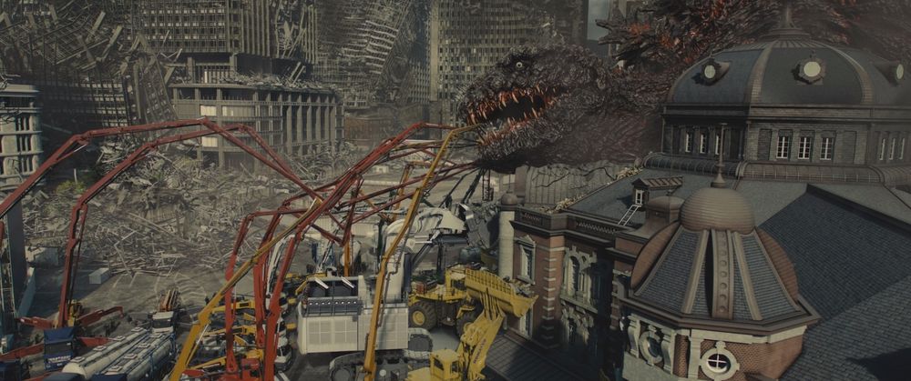 A frame from Shin Godzilla (2016).
Godzilla is laying down on some comfy buildings with a lot of rubble of a destroyed city in the background. About a dozen chemical/construction vehicles are in front of Godzilla's face and have long cranes and injection thingies going into Godzilla's mouth.

Not pictured: Godzilla's periodontist