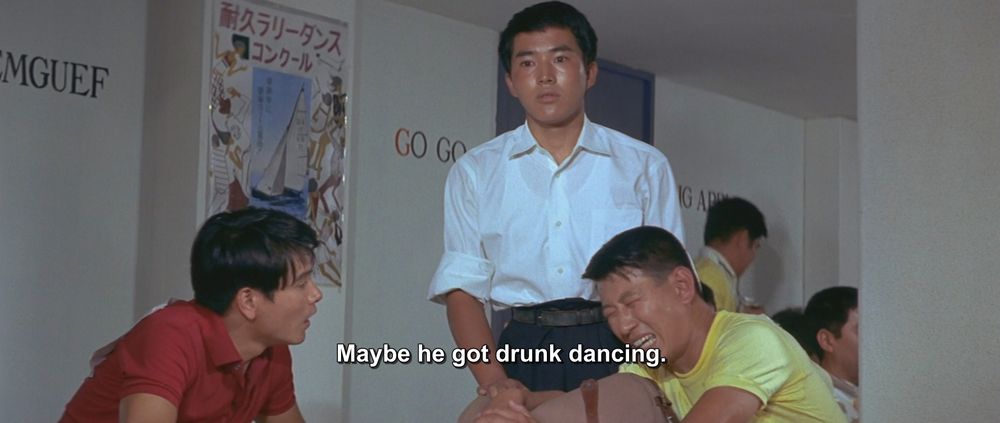 A frame from Ebirah, Horror of the Deep (1966). 
We see three men in a dance hall. Two of them are very sweaty and tired looking, sitting down, one in a red shirt and one in a yellow shirt, so they kind of have a Bert and Ernie thing going on if you ask me. The third man is standing, 1000 yard stare, wearing a white shirt (boring). In the background there is a poster with a sail boat on it as well as normal dancehall words on the walls, such as "GO GO," "BIG APPLE," and "MEREMGUEF"
The caption reads, "Maybe he got drunk dancing."

Not pictured: Godzilla; Ebirah; Meremguef(?); the dangers of drunk dancing