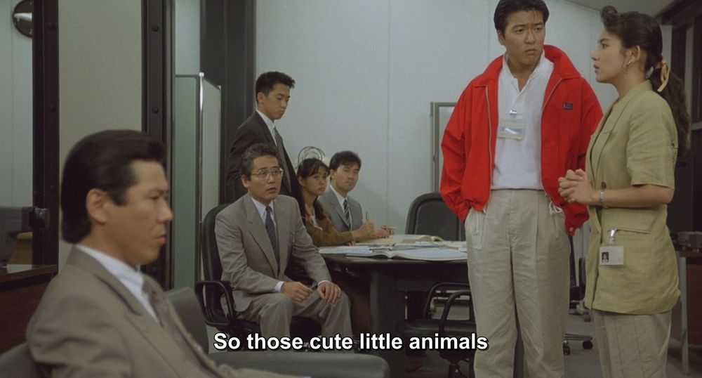 Two frames from Godzilla vs King Ghidorah (1991).
Several people are sitting in a boardroom of some kind. Most are sitting, a few are standing. One guy is wearing the reddest jacket ever devised. 
The caption reads, "So those cute little animals are now gigantic and savage?"

Not pictured: Godzilla; King Ghidorah; cute and savage animals