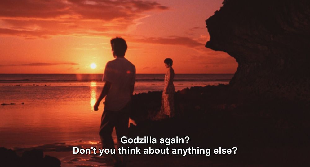 A frame from Godzilla vs Spacegodzilla (1994).
A man and woman stand on a rocky beach at sunset. The sky is all hues of orange and pink, the sun low on the horizon. The man stands closer to the camera, back to us. The woman is farther back, facing the ocean. She's wearing a pretty nice dress, he's just wearing a plain white tee and cargo shorts.
The caption reads, "Godzilla again? Don't you think about anything else?"

Not pictured: Godzilla; Spacegodzilla