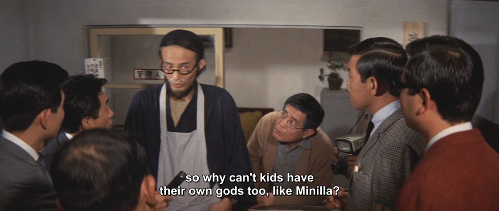 A frame from All Monsters Attack (1969).
A man in glasses and an apron speaks to a group of other men, huddled around him with cameras and microphones. He's got a look on his face like he knows he's about to drop some knowledge on these guys that will blow their minds.
The caption reads, "so why can't kids have their own gods too, like Minilla?"

Not pictured: the holy Lord Minilla, hallowed be Thy name