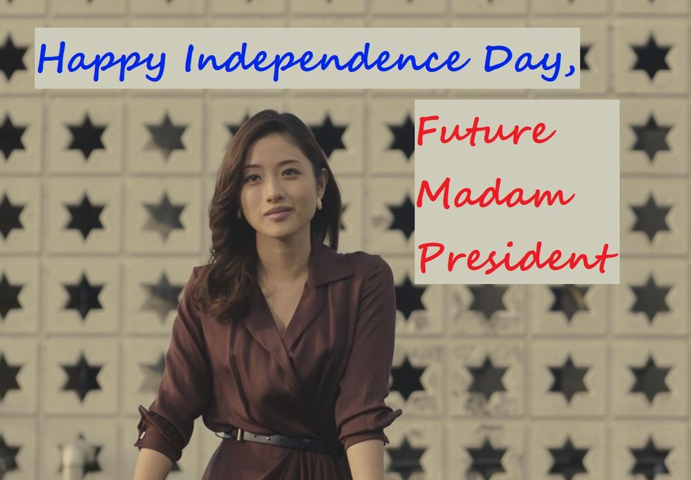 A frame from Shin Godzilla (2016).
A woman is standing outside in front of a backdrop of a beige wall that has numerous stars cut out of it. She is wearing a kind of flowy maroon pant suit, IDK I don't know clothes. She has a warm and contemplative smile on her face.
The words Happy Independence Day, Future Madam President have been added to the image in a script font.