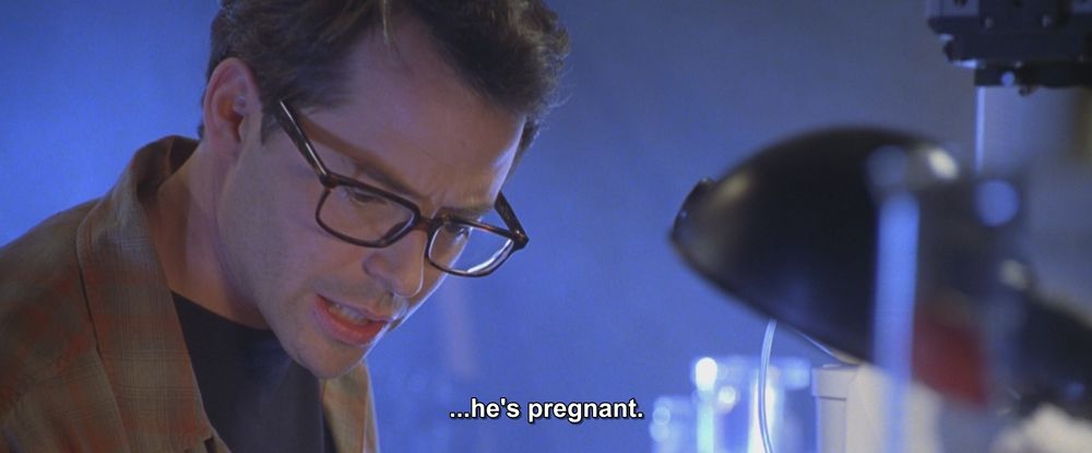 A frame from Godzilla (1998). 
A man wearing glasses and a... green? orange? brown? shirt is looking down at a bunch of sciency stuff like beakers.
The caption reads, "...he's pregnant."

Not pictured: Godzilla; all that mpreg art you commissioned of your comfort character