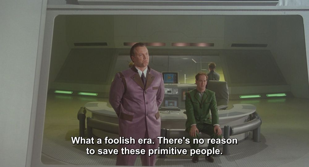 A frame from Godzilla vs King Ghidorah (1991).
Two men who look like the 1960's Joker and Riddler are in a futuristic room. One man is standing and dressed in an all purple suit and the other has red hair and is dressed in an all green suit.
The caption reads, "What a foolish era. There's no reason to save these primitive people." Very Riddler-esque statement if you ask me.

Not pictured: Godzilla; King Ghidorah; the Caped Crusader or the Boy Wonder