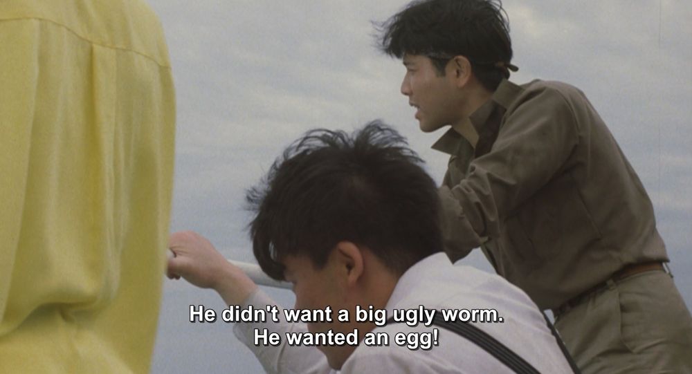 A frame from Godzilla vs Mothra (1992).
Some people are on a boat, grabbing onto the guard rail. They are looking out to the sea. One is hunkered down like the boat was just hit or is rocking violently.
The caption reads, "He didn't want a big ugly worm. He wanted an egg!"

Not pictured: Godzilla; Mothra; big ugly worms or eggs