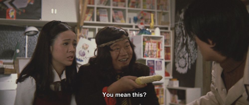 The hippie is now smiling and pointing a half-eaten corncob at the man in the trenchcoat.
The caption reads, "You mean this?"

Not pictured: Godzilla; Gigan

I never realized he was holding corn in this scene.