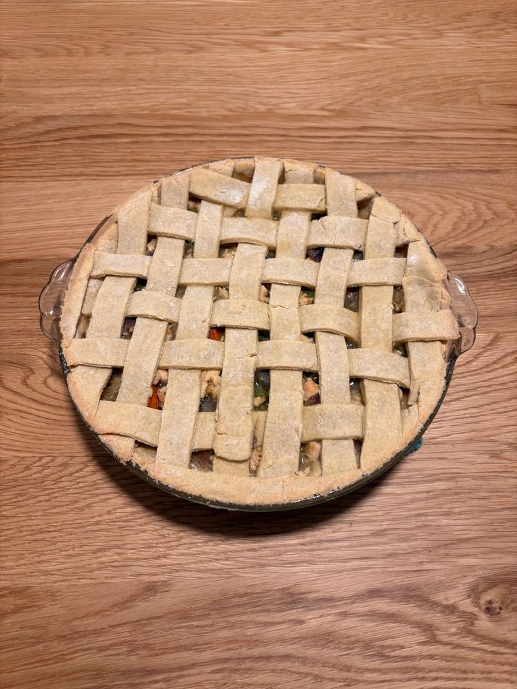 A lattice top pie sits on a wood stain tabletop. Some of the lattice is not perfect and doesn’t weave back and forth, skipping one of the pastry strips at the bottom.