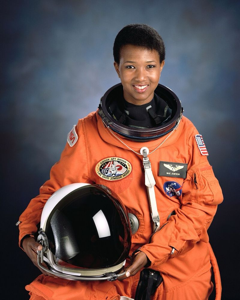Mae Jemison wears a bright orange NASA space suit and holds her helmet for a photo 