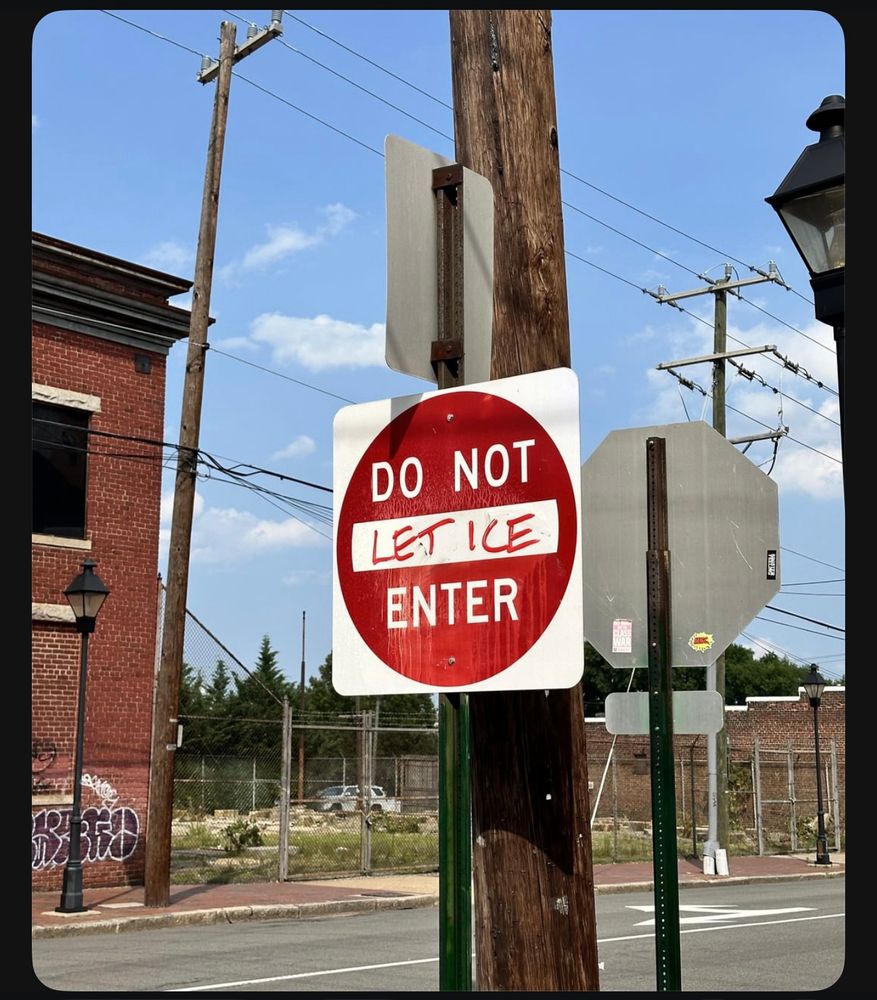 A Do Not Enter sign on an urban block has red handwritten text in the center that makes the sign read Do Not Let Ice Enter
