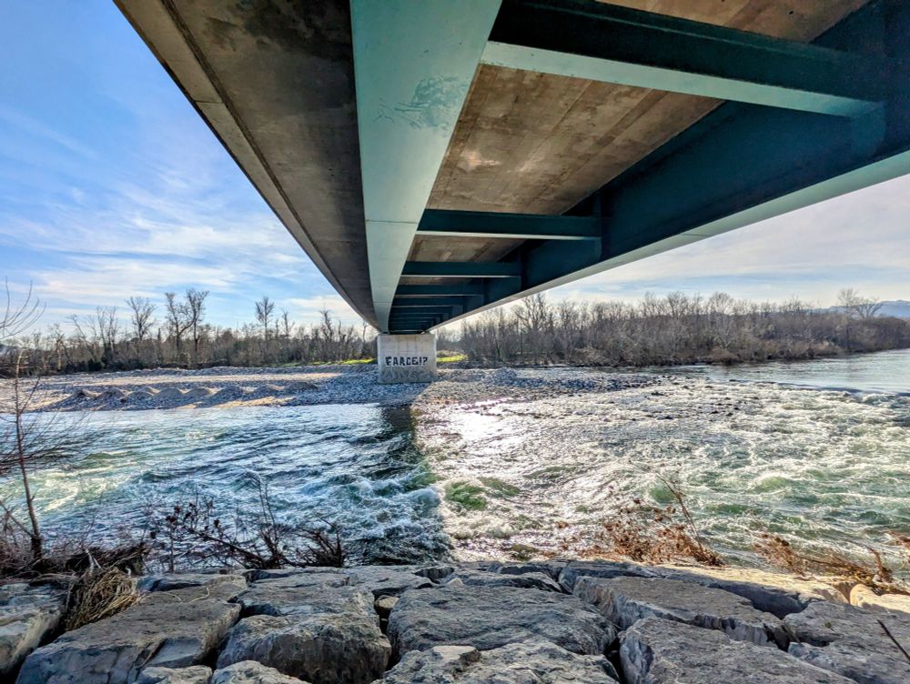 Graffiti avec l'inscription Farce ? en noir sur un pilier de pont avec la rivière de l'Ardèche et le pont de loin