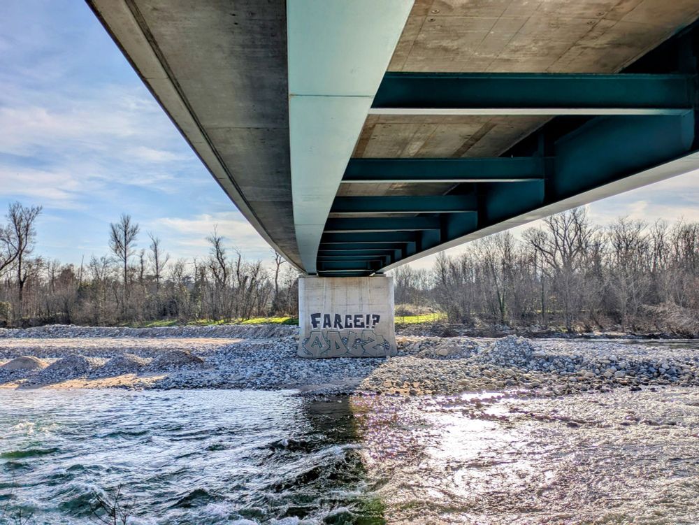 Graffiti avec l'inscription Farce ? en noir sur un pilier de pont avec la rivière de l'Ardèche et le pont