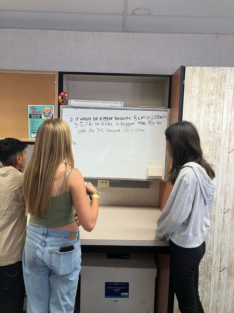 Three students at whiteboards discussing math