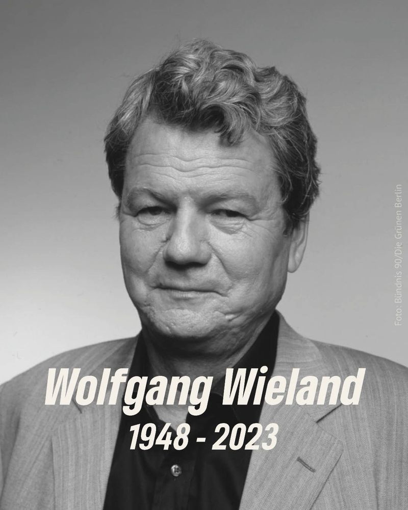 Schwarz-weiß Porträt von Wolfgang Wieland. Er trägt Hemd und Jacket, sein kurzes Haar ist ordentlich frisiert. Sein Blick ist ernst. Unter im in weiß der Text: „Wolfgang Wieland, 1948-2023“