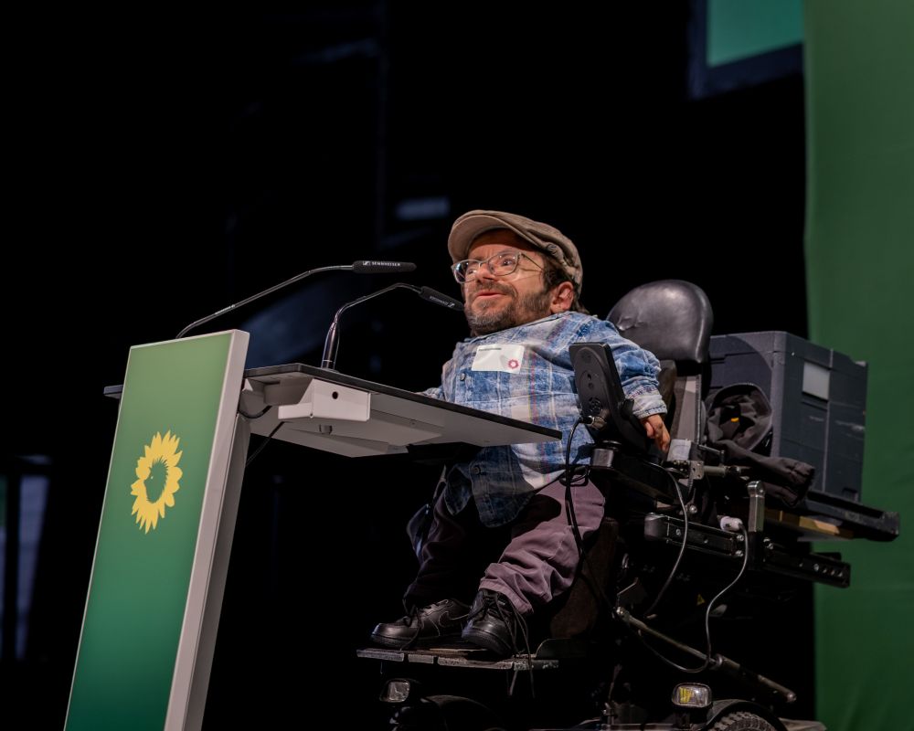 Raul Krauthausen spricht am Redepult des Stadtkongress. Das Redepult und der Hintergrund sind grün gebrandet und eingefärbt. 
