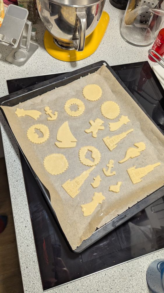 Backblech mit Backpapier und verschiedenen Mürbeteig Plätzchen drauf.