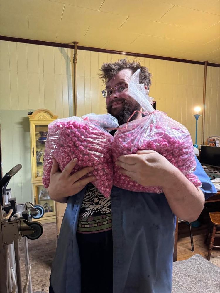 An exhausted rpg creator holds two large sacks of pink d12s from the TTRPG Tombpunk 