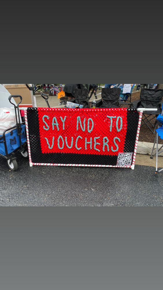 A large protest sign that is made of a net and yarn that reads, “Say no to vouchers”