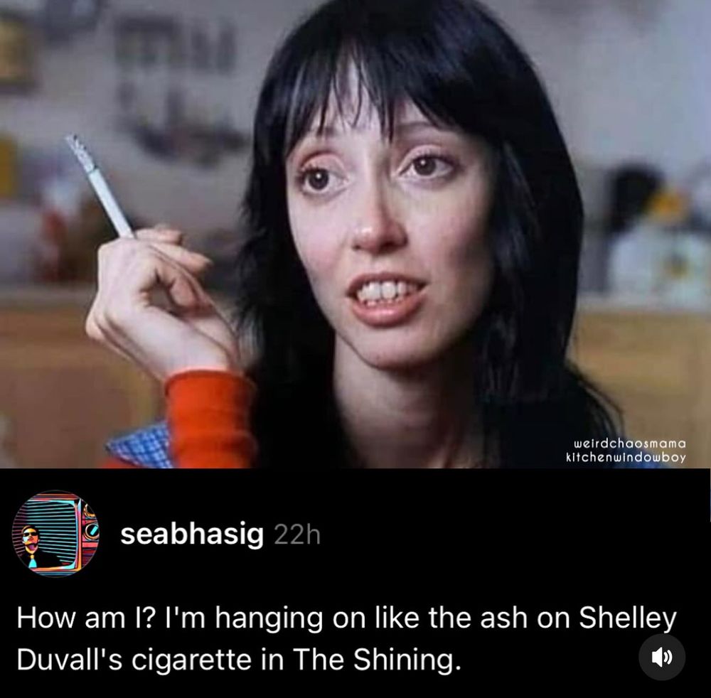 A still from The Shining showing Shelley Duval holding a cigarette with a long head of unbroken ash with the caption: “How am I? I’m hanging on like the ash on Shelley Duvall’s cigarette in The Shining” 
