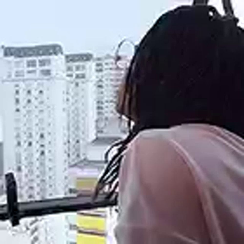 a woman wearing headphones is riding a ferris wheel in front of tall buildings .