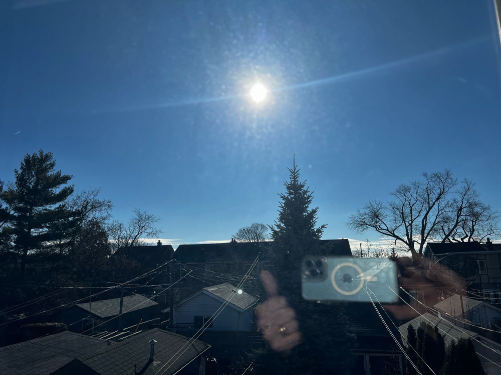 Sunny and clear blue sky with houses and trees on the horizon and reflection showing thumbs up