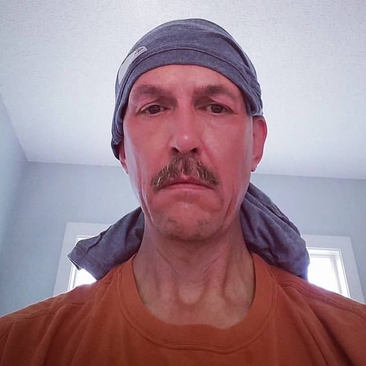 selfie of me in an orange t-shirt after a long run. I have a gray shire wraped around my head and tied behind like a bandana and I do not look happy.