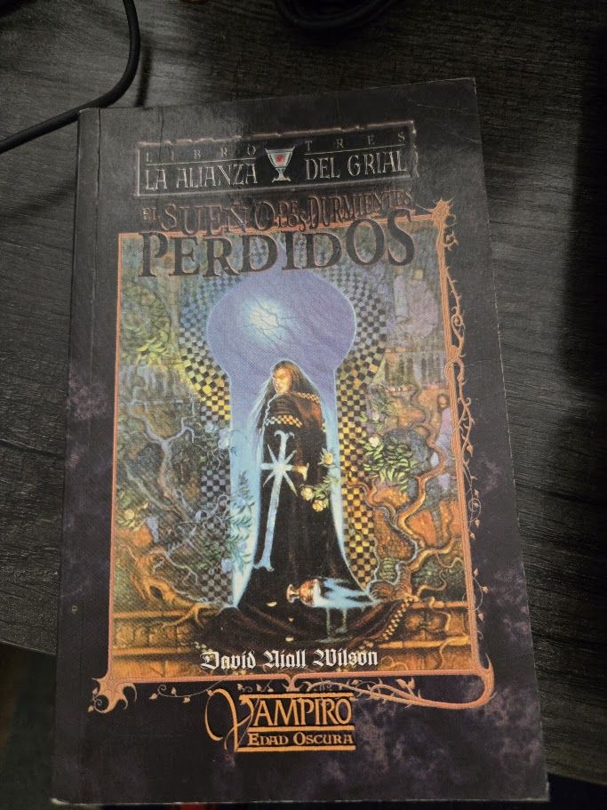 The Spanish edition of the third book in my Grails Covenant Trilogy - El Sueno de loss Dormientes Perdidos The vapire Montrofant, in a dark robe with a silver cross running up it's length. Tow either side are maps, and he is standing in a giant door that is shaped like a keyhole.