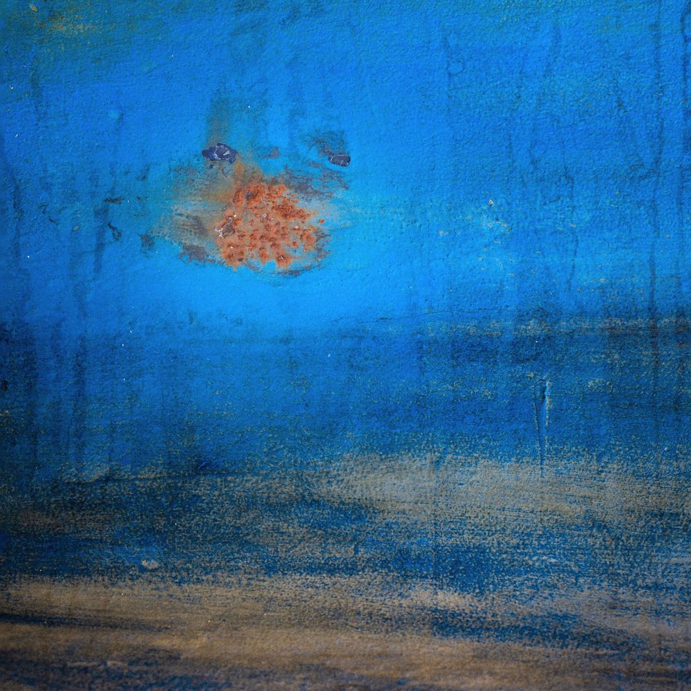 An orange rust spot on the hull of a blue yacht.