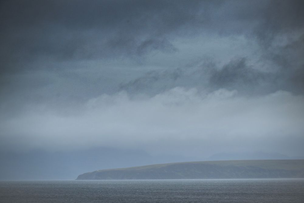 A headland in the far distance shrouded in mist and rain, with heavy clouds overhead.