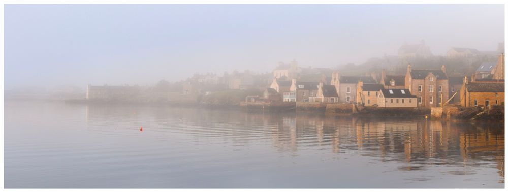 A view of all the houses on the edge of Stromness harbour, disappearing into a bank of sea fog.