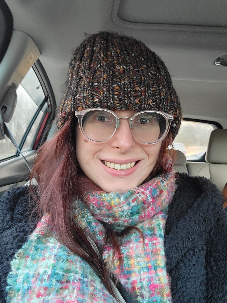 Girl with red hair and froot loop scarf smiles in the passenger seat of a car