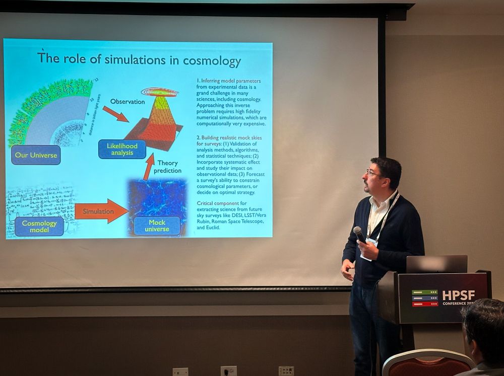 Presenter holding a microphone stands next to a projection screen displaying a slide titled "The role of simulations in cosmology," which includes diagrams and text about cosmology models, simulations, and mock universes.