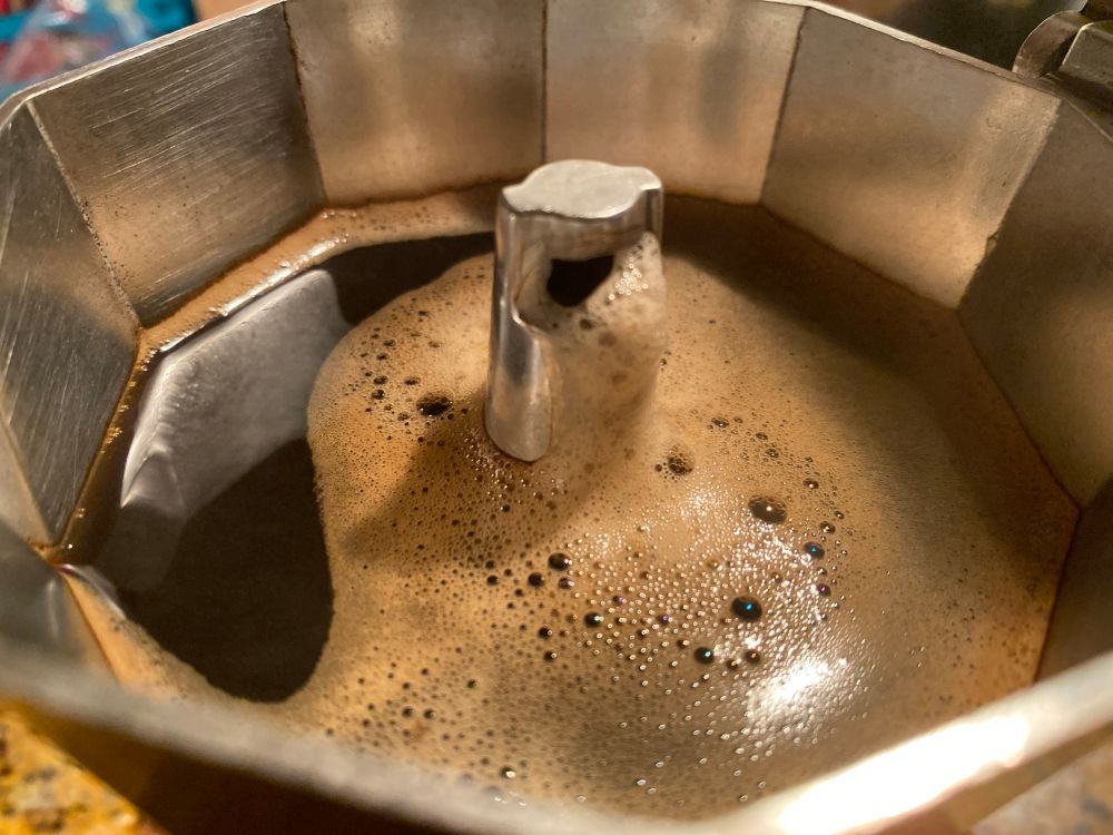 Café y espuma saliendo de una cafetera italiana. Atmósfera cálida.