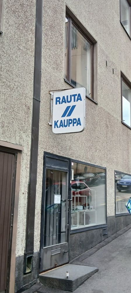 Kivijalkarautakauppa. Oven päällä tyylikäs valkoinen kyltti, jossa sinisellä teksti RAUTA // KAUPPA.