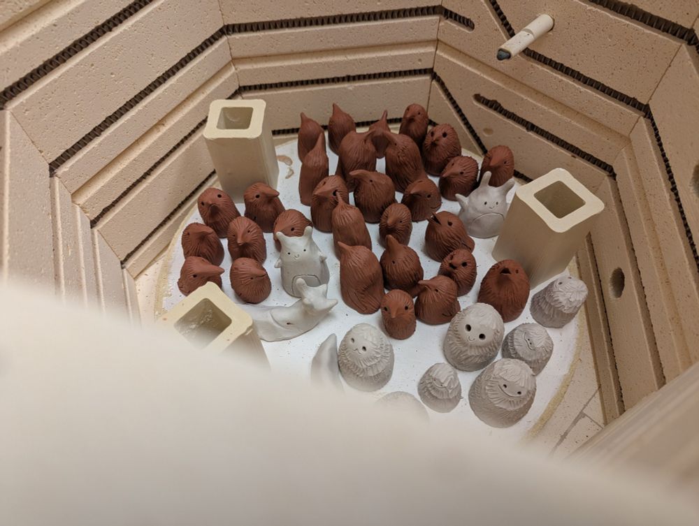 Many small sculptures - mostly little crows - are nestled together inside of a kiln.