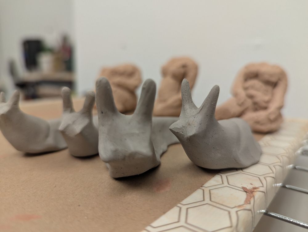 Four freshly made clay slugs sit on top of a brown board. Three figure studies are blurry behind them.