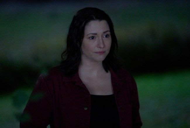 A woman standing, looking at something 