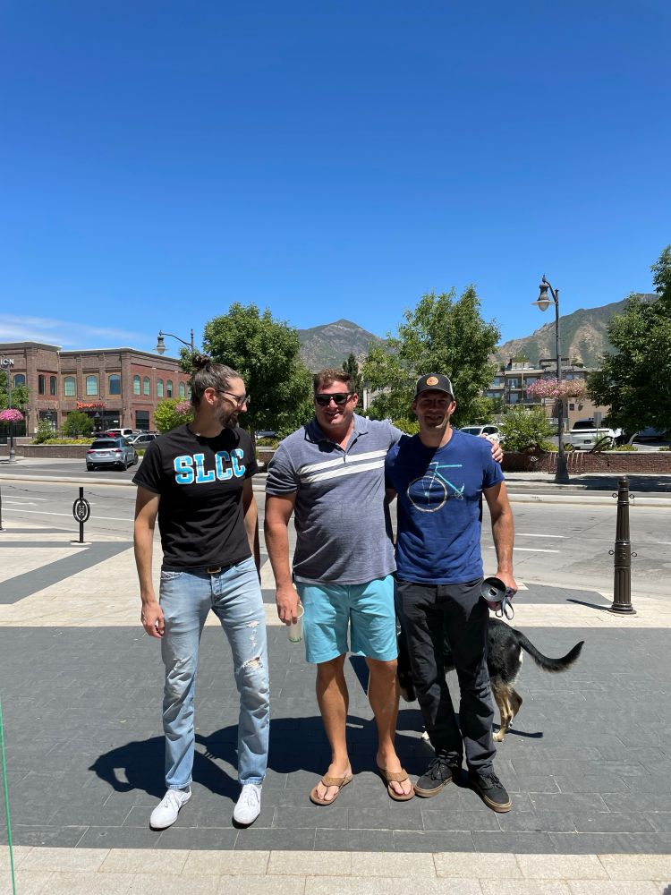 Three middle-aged men in casual clothes with a dog half visible behind one of them