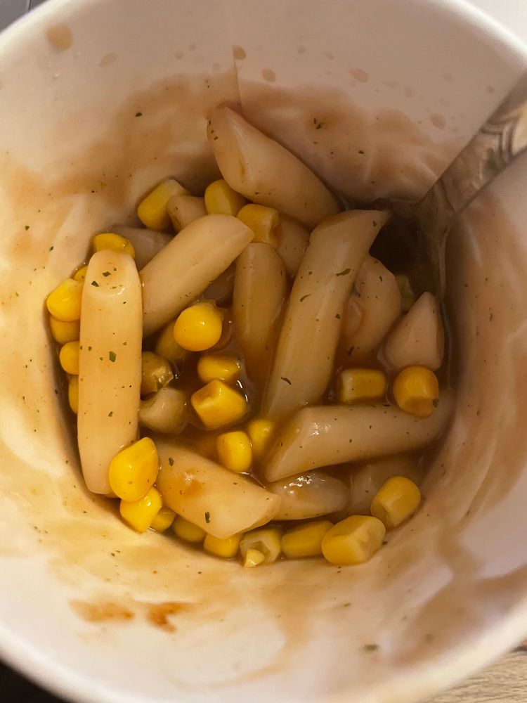 Pappbecher mit Instant-Tteokbokki in bräunlicher Sauce und Dosenmais