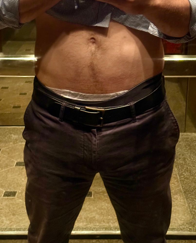 A selfie from inside an elevator with mirrored walls. I’m holding up my shirt so the waistband of my goodnite is visible. 