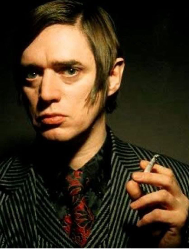 Blixa Bargeld looking stern, holding a cigarette