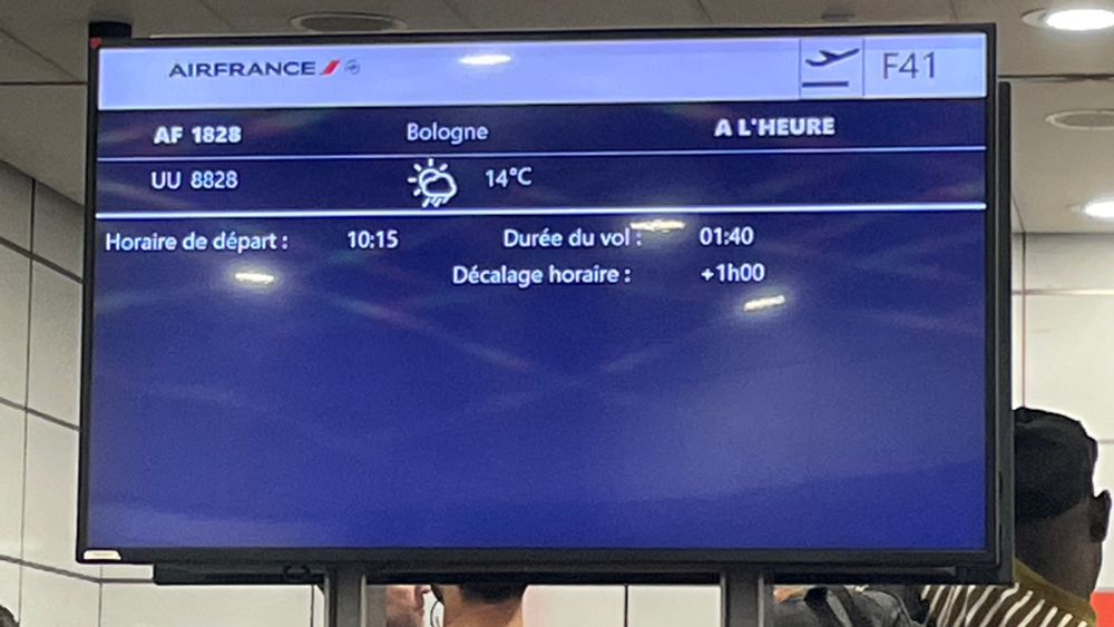Panneau d’information à l’aéroport indiquant un vol pour Bologne. Durée du vol 1h40, décalage horaire +1h00