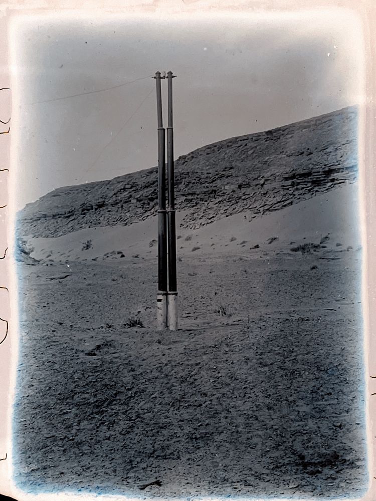 Un poteau de télégraphe dans le désert (il s’agit de deux poteaux côte-à-côte). Chaque poteau est composé de plusieurs parties. 