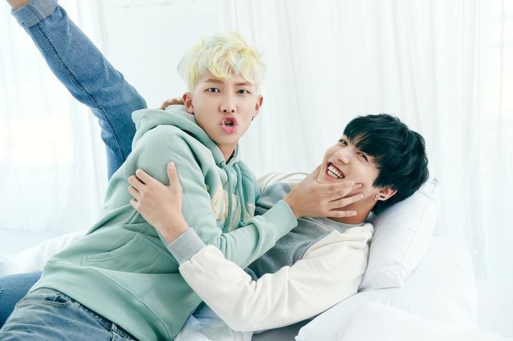 2015 seasons greetings Namkook. Jungkook is lying on a white couch, laughing, with one leg up (go go gymnastics) - his other leg lying down. Namjoon is half lying on him and pinching his dimples; he makes a big pout/grimace at the camera