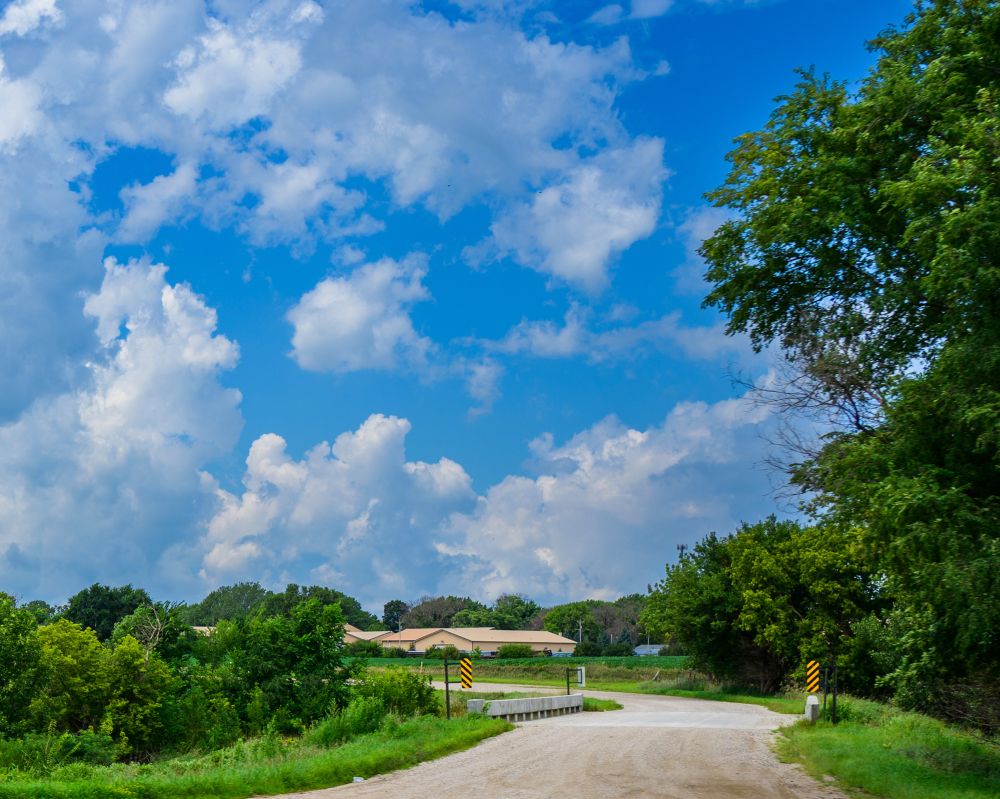 A country road leading to a small town with fluffy clouds over head.