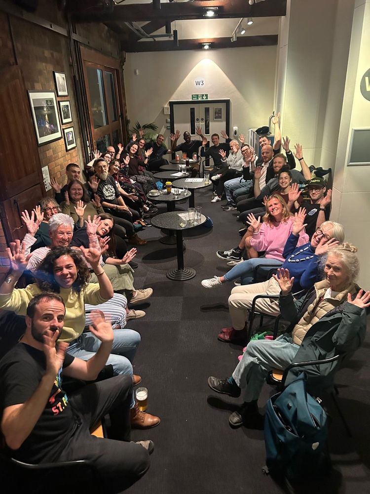 32 of us sitting on the chairs with 4 tables in the room with white and bricked walls. Hands waving that signifies applauding to the film!