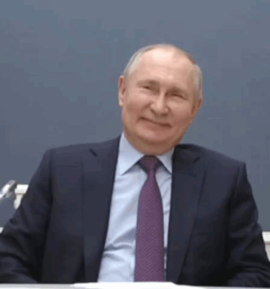 a man in a suit and tie is smiling while sitting at a desk .